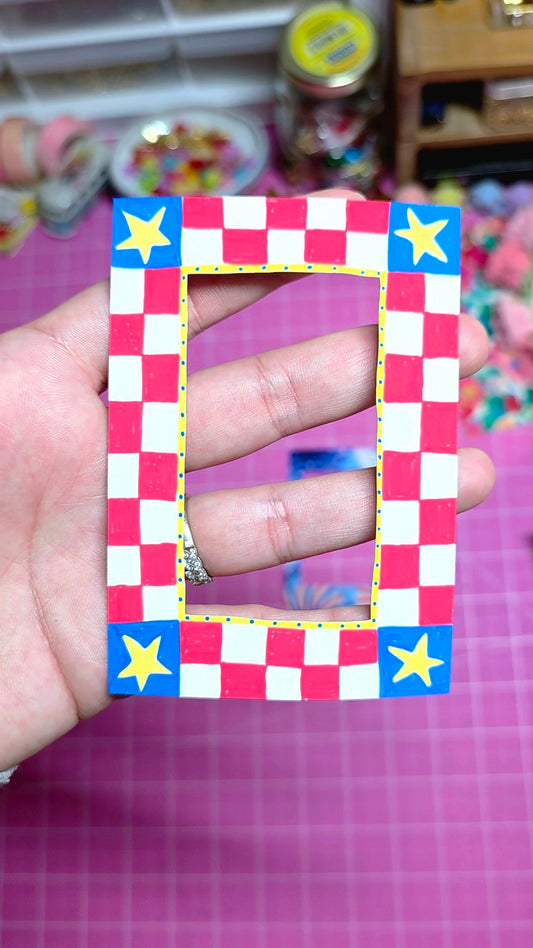 Hand holding a checkered frame with stars on a pink background