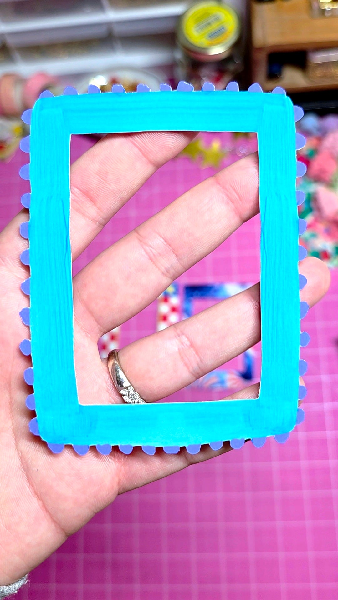 Hand holding a blue textured frame against a pink background