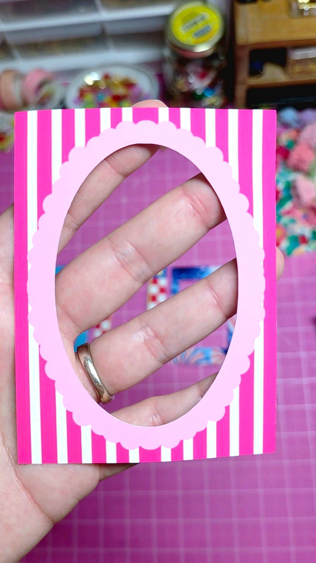 Hand with a ring on a pink and white striped card against a colorful background