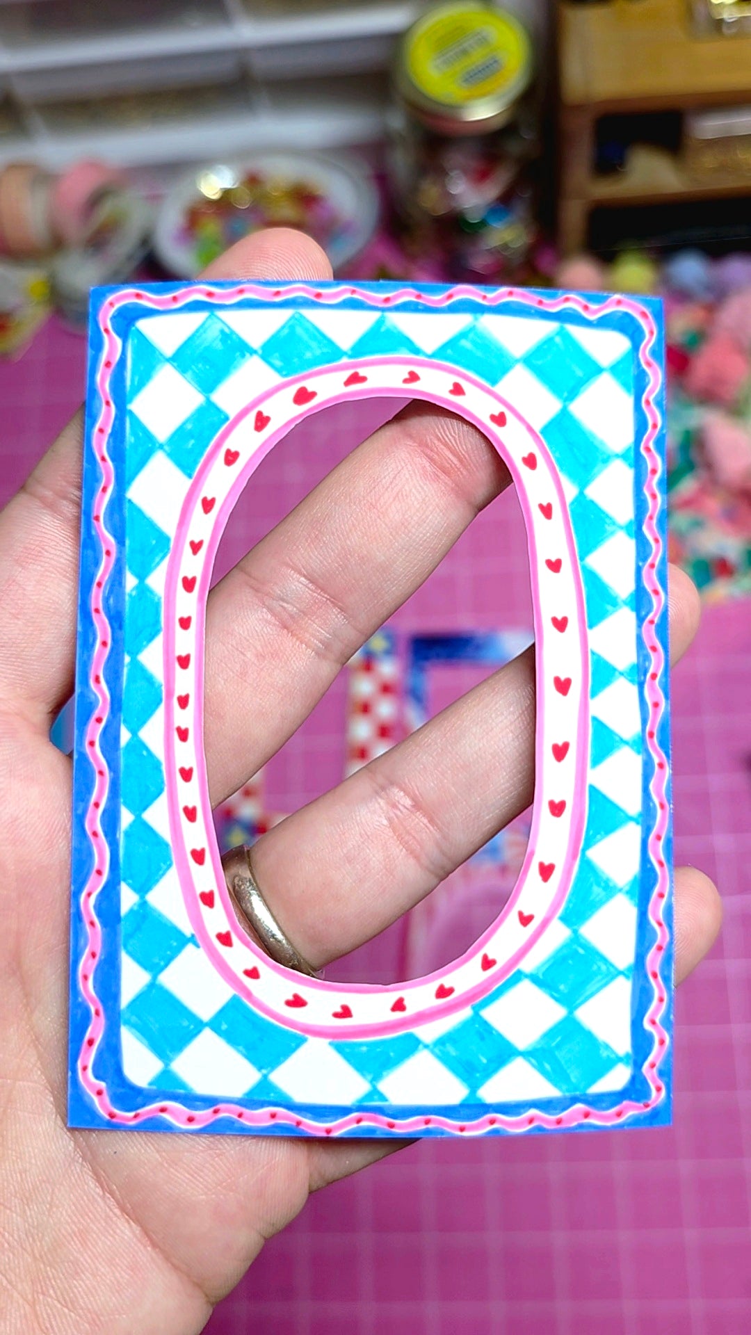 Hand holding a decorative letter 'D' with a blue and pink checkered border.