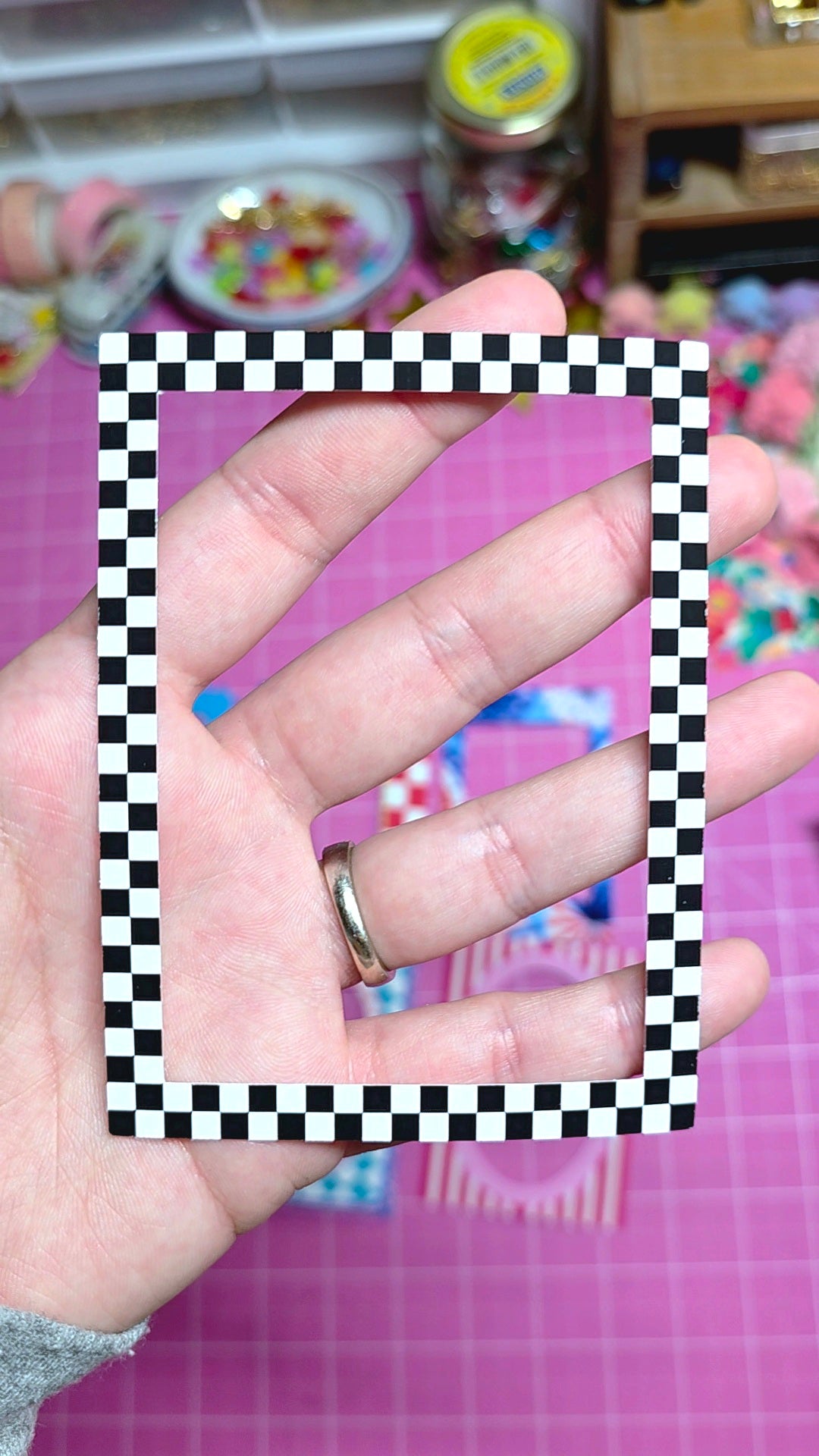 Hand holding a black and white checkered frame against a colorful background
