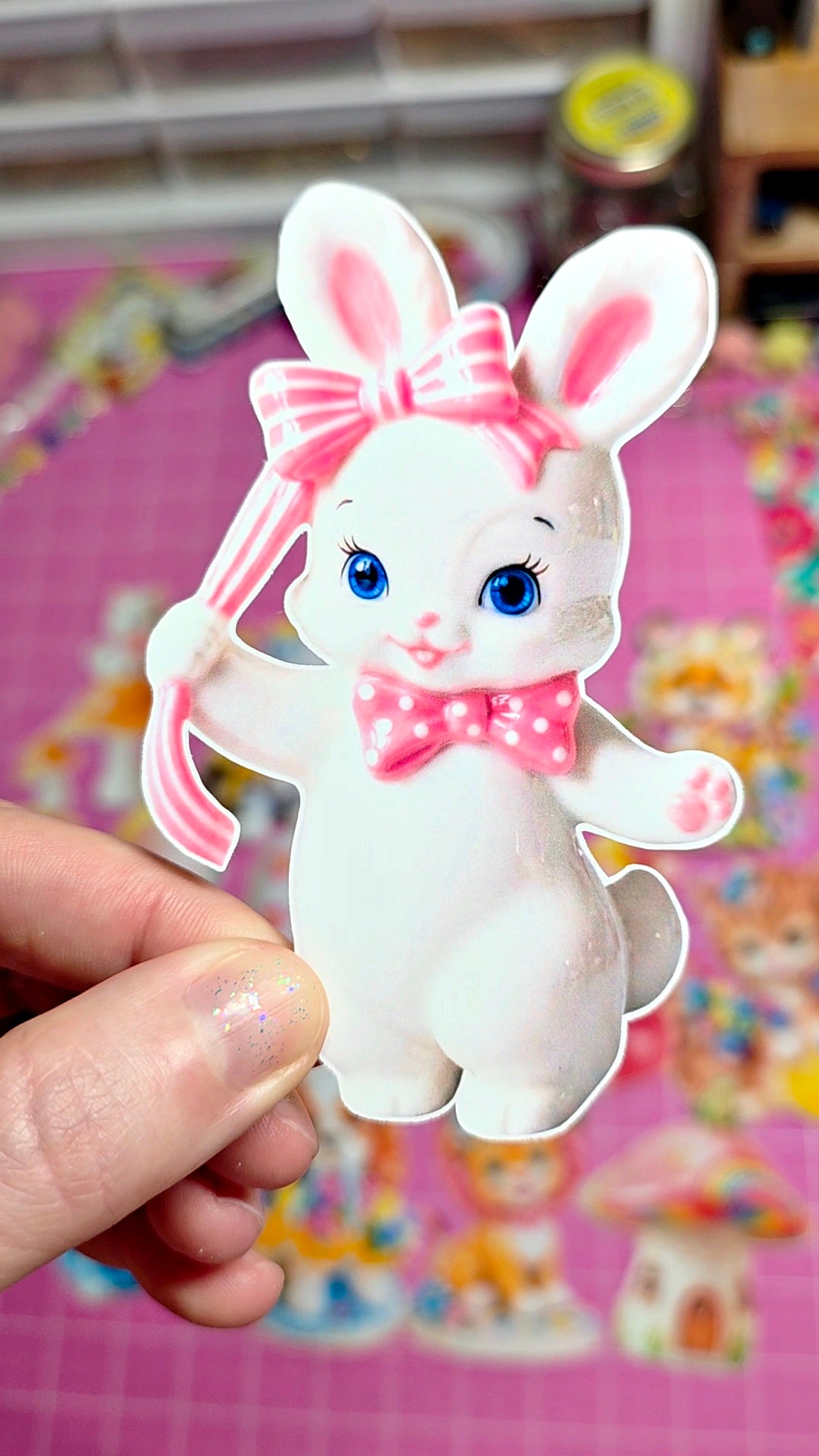Cartoon rabbit character with a pink bow held by a hand on a colorful background