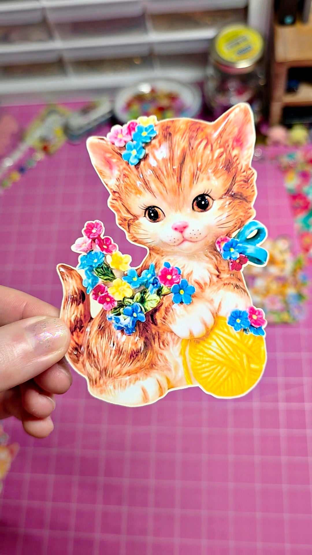 Sticker of a cat with flowers held over a pink grid background