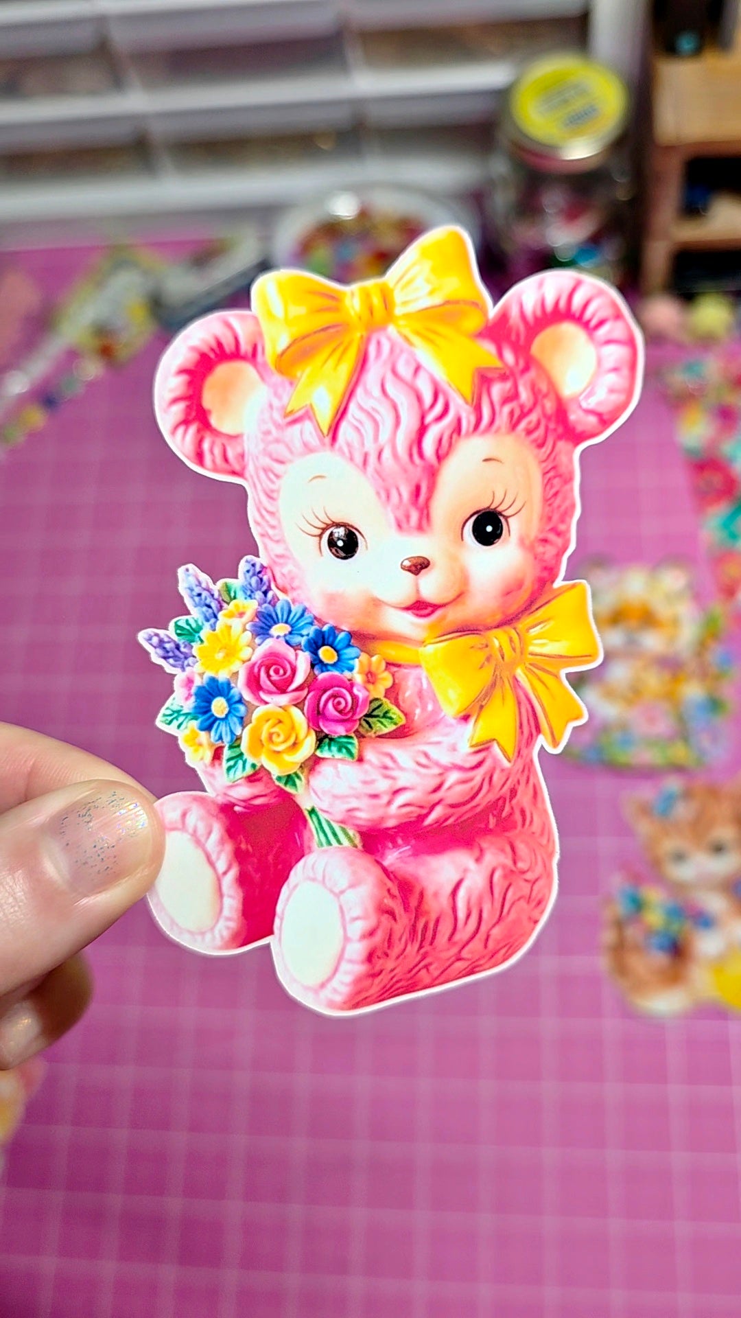 Pink bear with a yellow bow holding flowers on a pink background