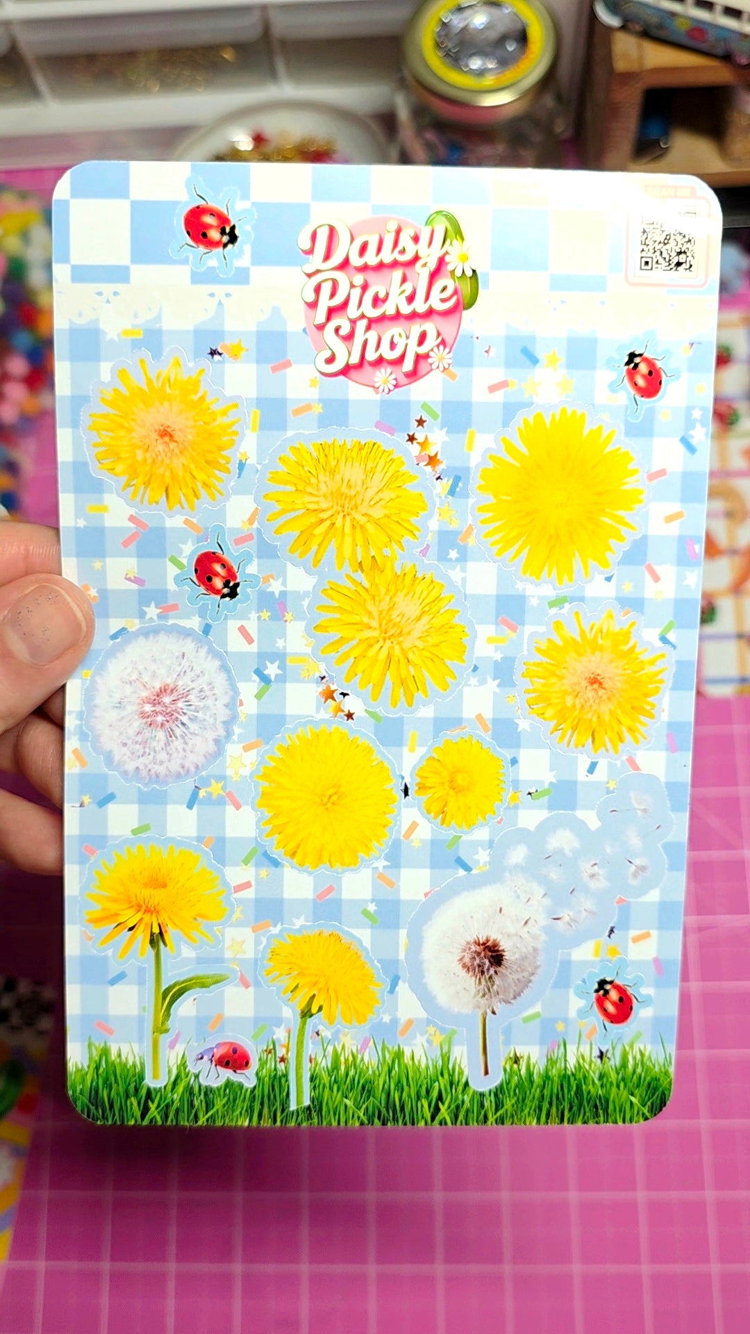 Sticker sheet with yellow flowers and ladybugs on a blue checkered background, held by a hand.