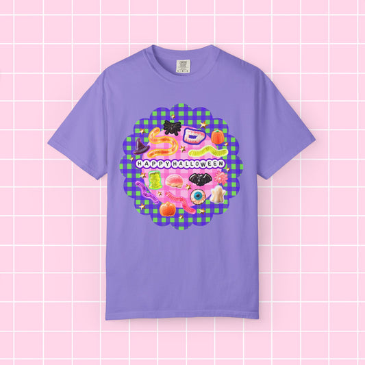 A lavender purple short-sleeve t-shirt with a colorful 'Happy Halloween' graphic on the chest, displayed flat against a pink grid background.