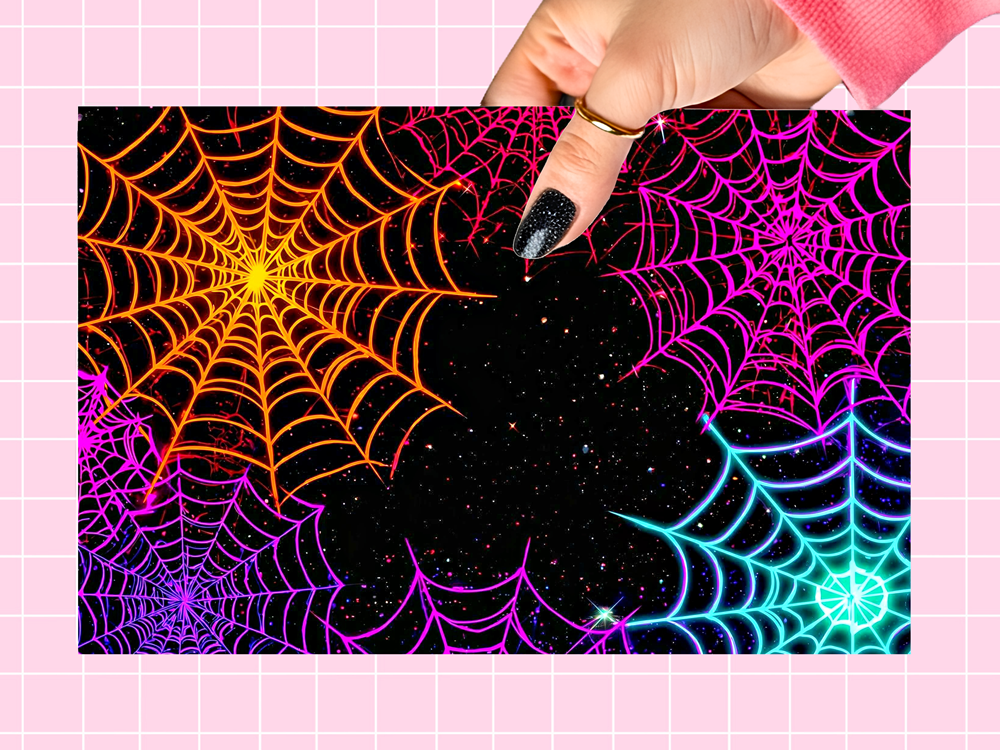 A rectangular art print featuring neon-colored spiderwebs on a black starry background, held by a hand against a pink grid backdrop.