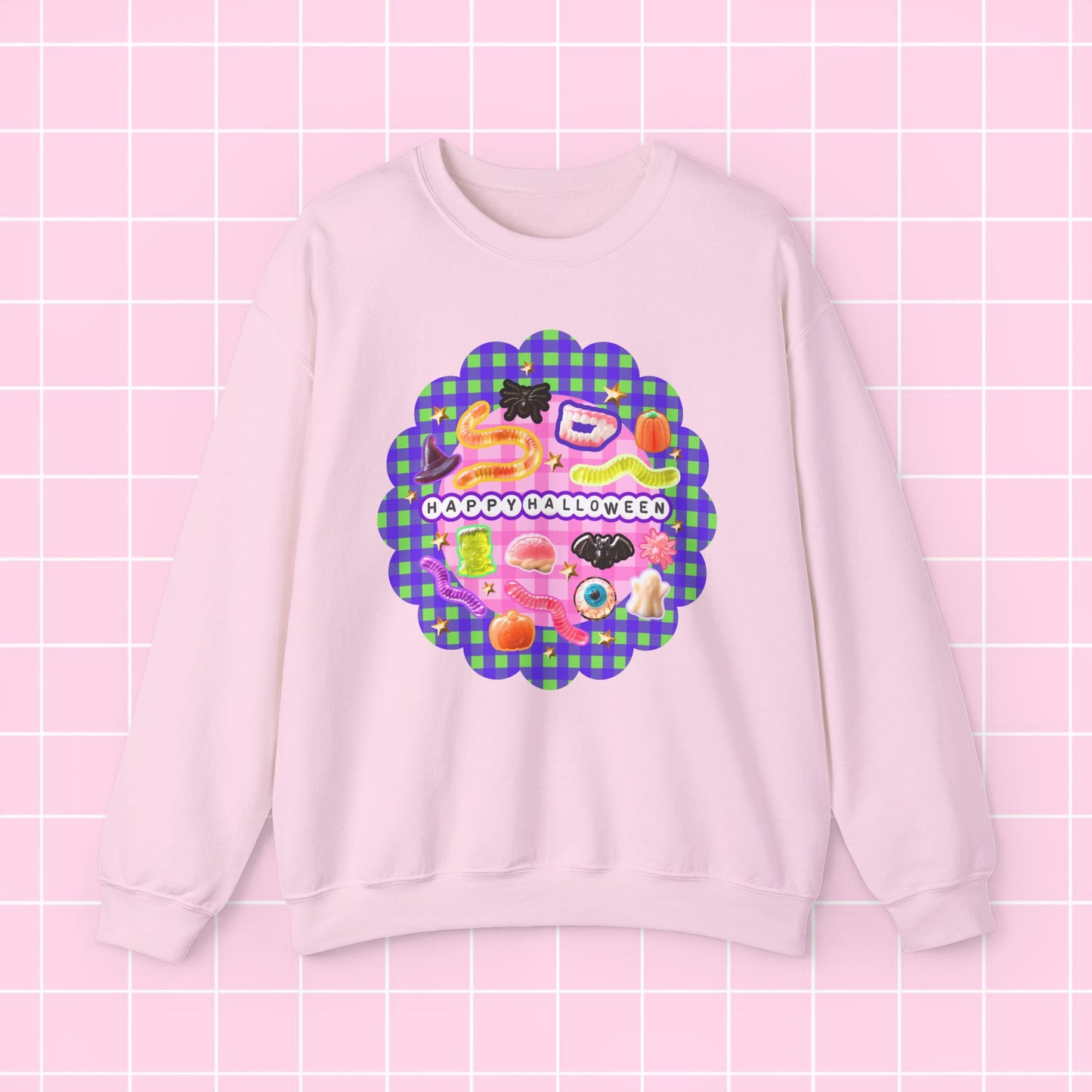 A light pink crewneck sweatshirt featuring a colorful retro graphic with the text 'HAPPY BIRTHDAY' on a purple and green plaid scalloped background, displayed against a pink grid backdrop.