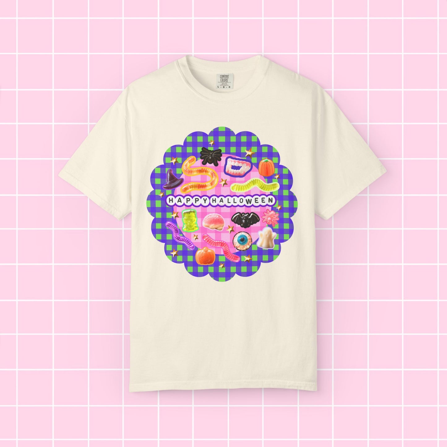 A cream-colored short-sleeve t-shirt with a colorful 'Happy Halloween' graphic on the front, displayed against a pink grid background.