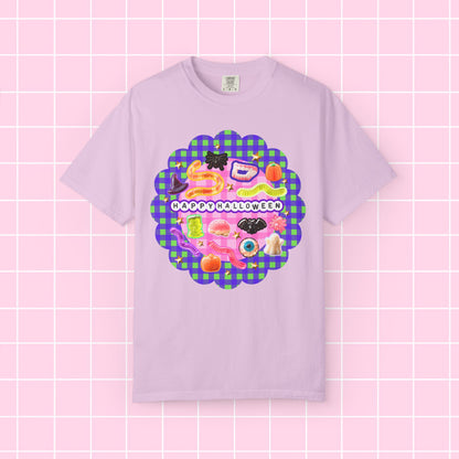 A light purple short-sleeve t-shirt with a colorful 'Happy Halloween' graphic on the chest, displayed against a pink grid background.