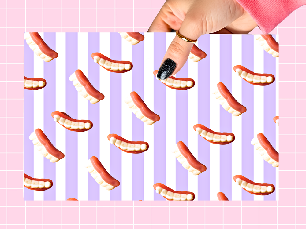 A hand with black glitter nail polish holds a rectangular sheet featuring a repeating pattern of pink and white striped tooth grins on a pastel pink grid background.