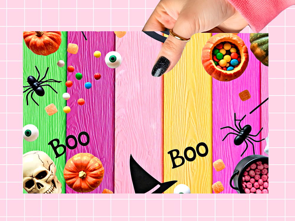 A Halloween-themed decorative sign or backdrop featuring vertical pastel wood planks in green, pink, light pink, and yellow, decorated with pumpkins, candy canes, black spiders, eyeballs, a witch hat, and the word 'BOO'. A hand with black glitter nail polish is shown at the top right holding a small black object, against a pink grid background.