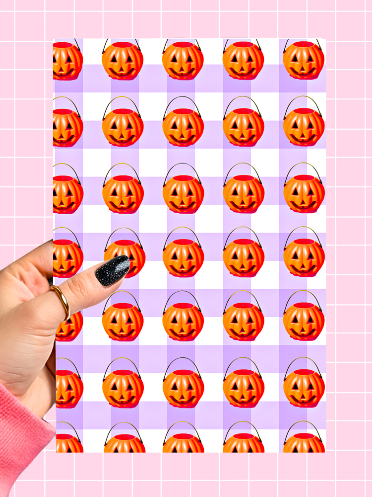 A sheet of Halloween candy bucket stickers featuring orange jack-o'-lantern pumpkins on a lavender and white checkerboard background, held by a hand with glittery black nail polish against a pink grid backdrop.