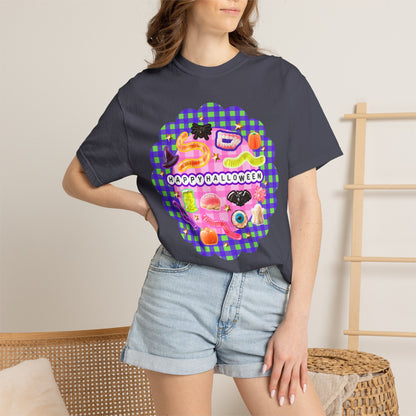 A woman wearing a dark charcoal gray t-shirt with a colorful 'Happy Halloween' graphic print featuring candy and sushi illustrations, paired with light-wash denim shorts in a cozy indoor setting.