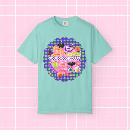 A mint green short-sleeve t-shirt with a colorful 'Happy Halloween' graphic on the chest, displayed against a pink grid background.