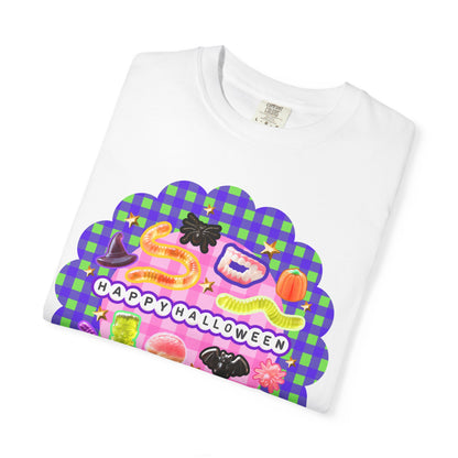 A white short-sleeve crewneck T-shirt folded flat, featuring a colorful 'Happy Halloween' graphic print with a purple and green plaid background and cartoon candy and spider motifs.