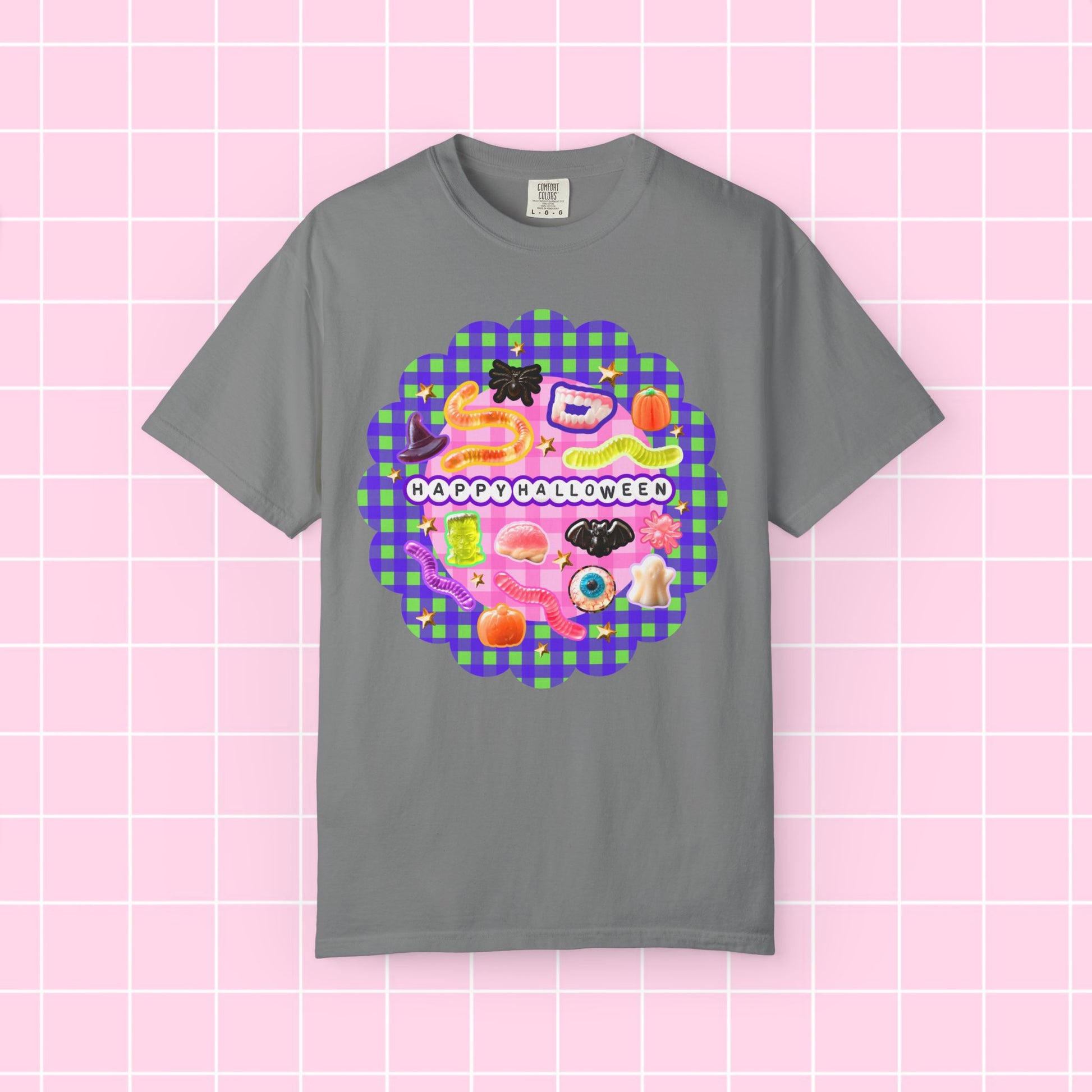 A gray short-sleeve crewneck t-shirt featuring a colorful 'Happy Halloween' graphic print on the front, displayed against a pink grid background.