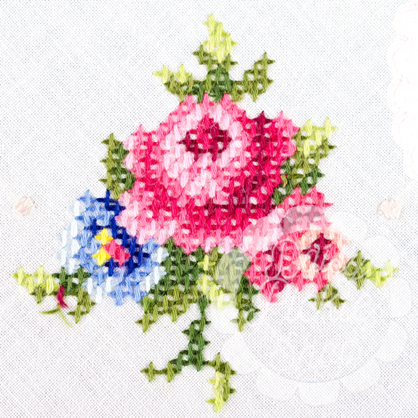 Cross-stitched design of pink flowers with green leaves on a white background