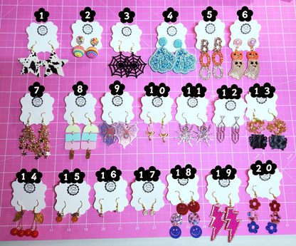 Assorted earrings on numbered cards against a pink grid background
