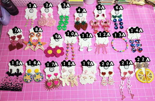 Assorted earrings on a pink surface with labels