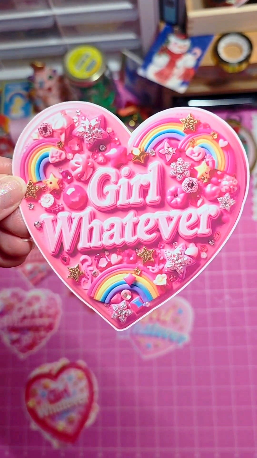 Heart-shaped pink sticker with 'Girl Whatever' text and decorative elements on a pink background.