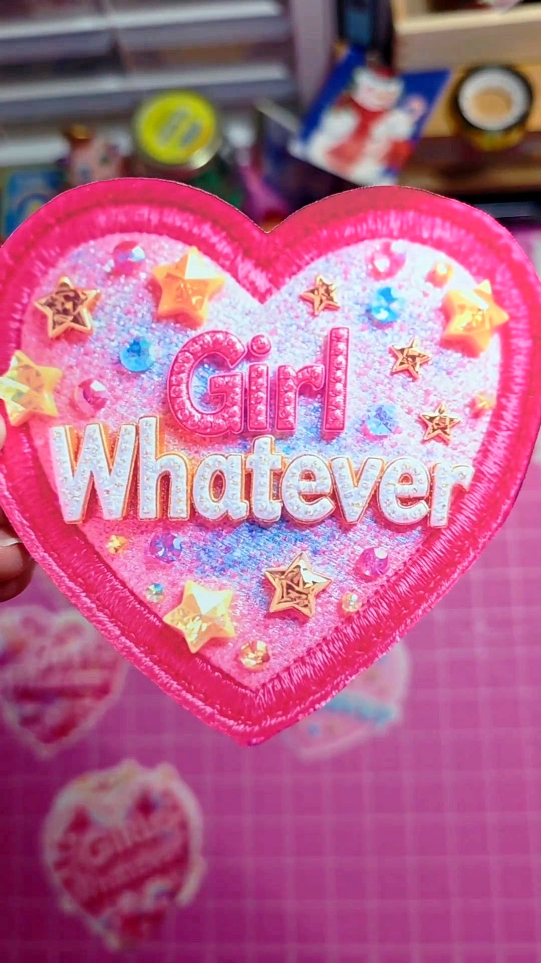 Heart-shaped patch with 'Girl Whatever' text on a pink background