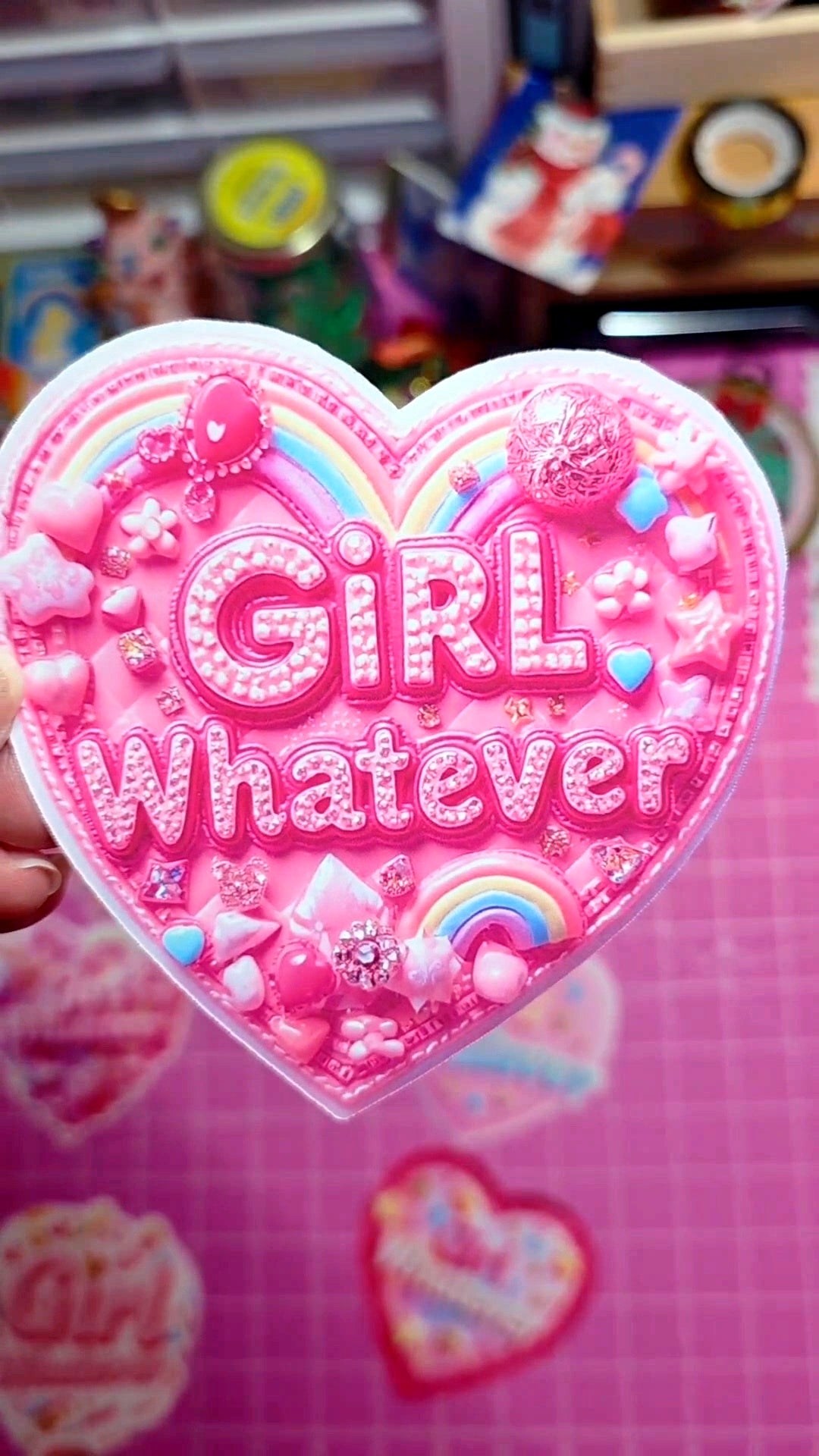 Heart-shaped pink sticker with 'Girl Whatever' text and decorative elements on a colorful background.
