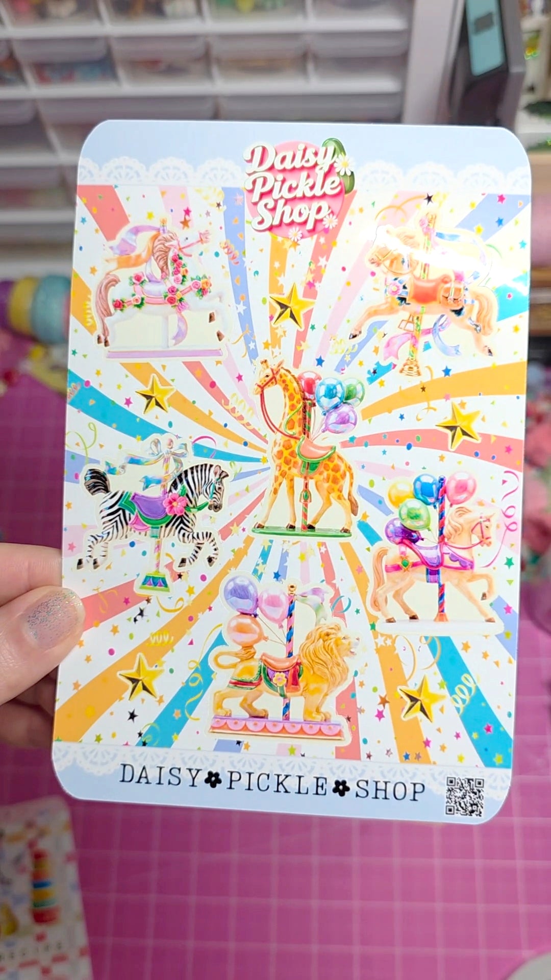 Colorful card with cartoon characters and 'Daisy Pickle Shop' branding held by a hand on a pink grid background.