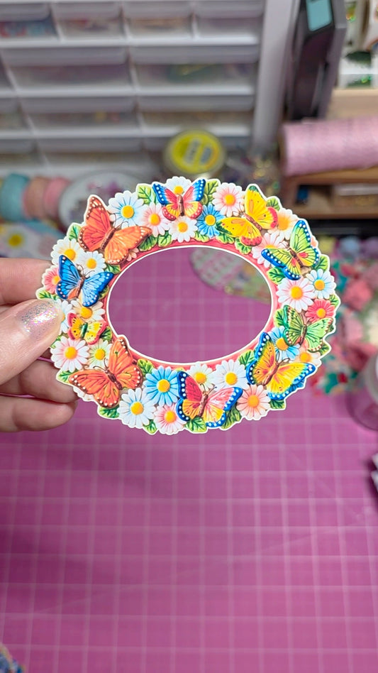 Colorful butterfly and flower design on a circular frame held by a hand.