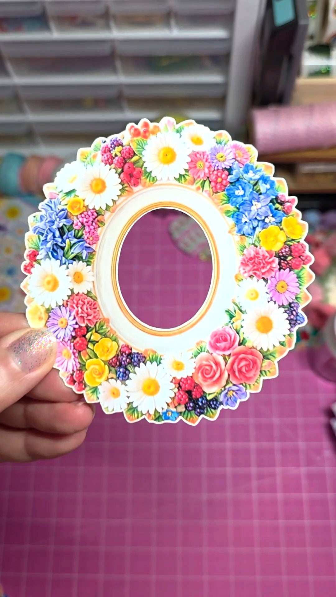 Decorative photo frame with colorful flowers held by a hand on a grid background