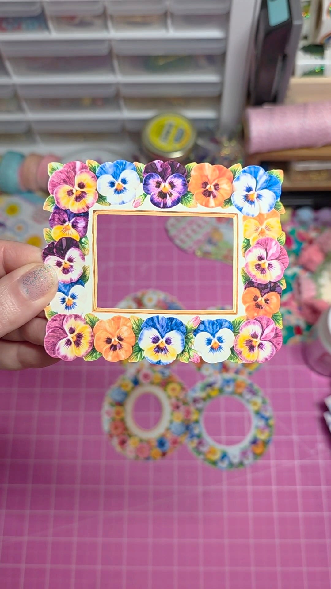 Colorful flower-shaped picture frame held by a hand on a pink grid background.