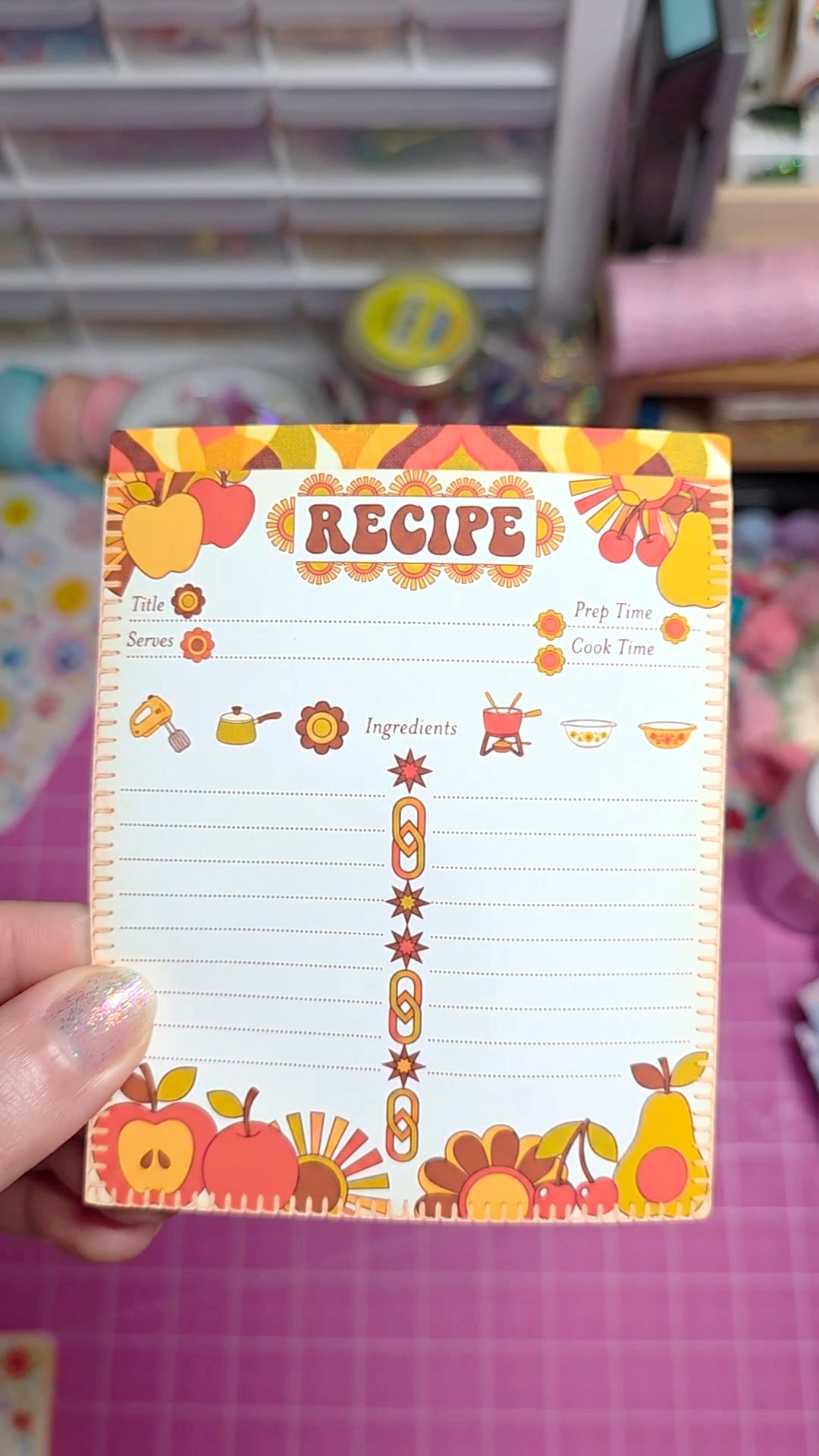 Recipe card with colorful design held by a hand on a pink background