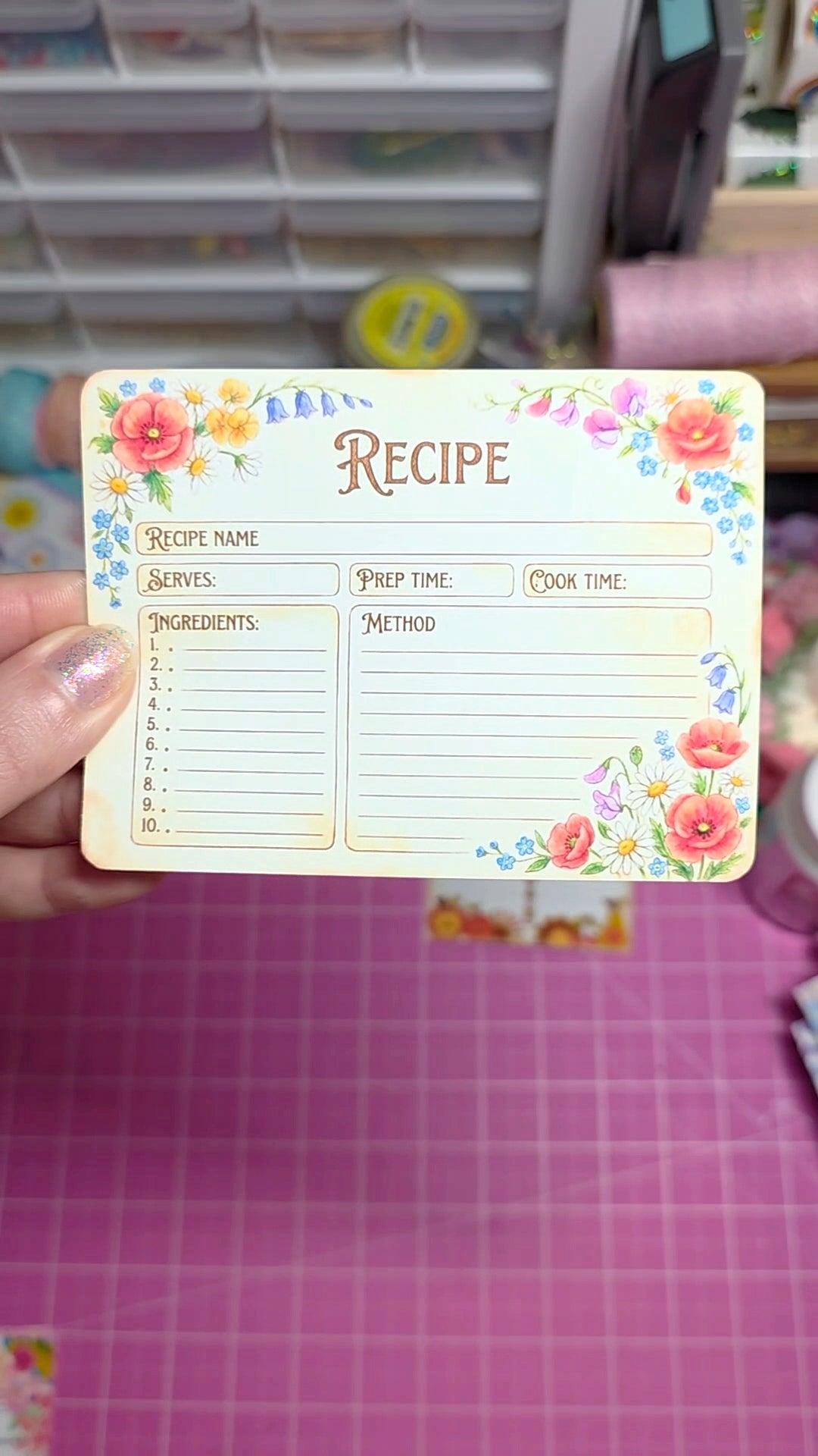 Floral recipe card held by a hand with a pink grid background