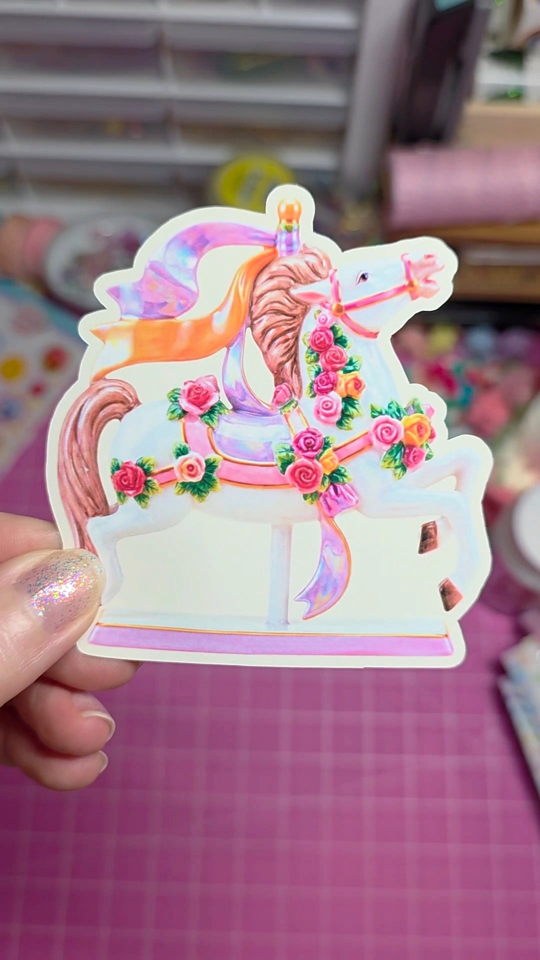 Decorative sticker of a carousel horse with flowers held by a hand on a checkered background.