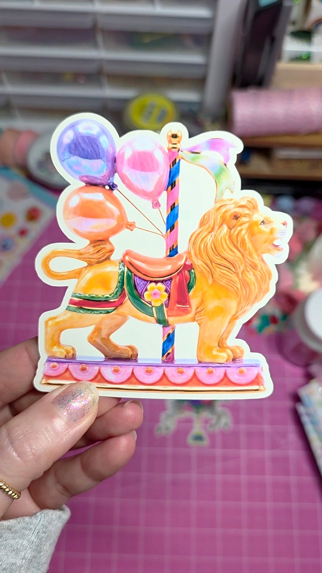 Colorful lion and carousel sticker held by a hand with a blurred indoor background