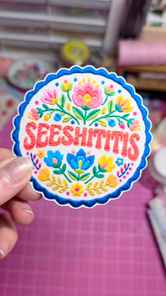 Colorful 'SEESHITITIS' sticker held by a hand on a pink background