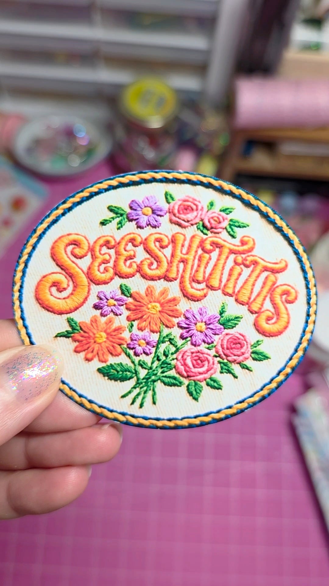 Circular embroidered patch with 'Seeshiiiii' text and floral designs held by a hand.