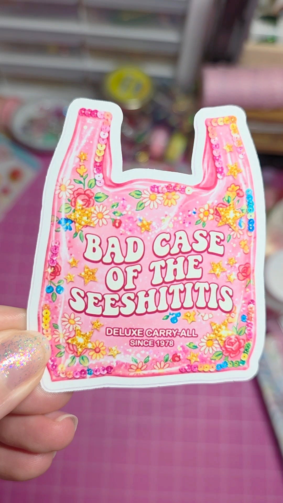 Pink plastic bag with floral design and text held by a hand against a blurred background