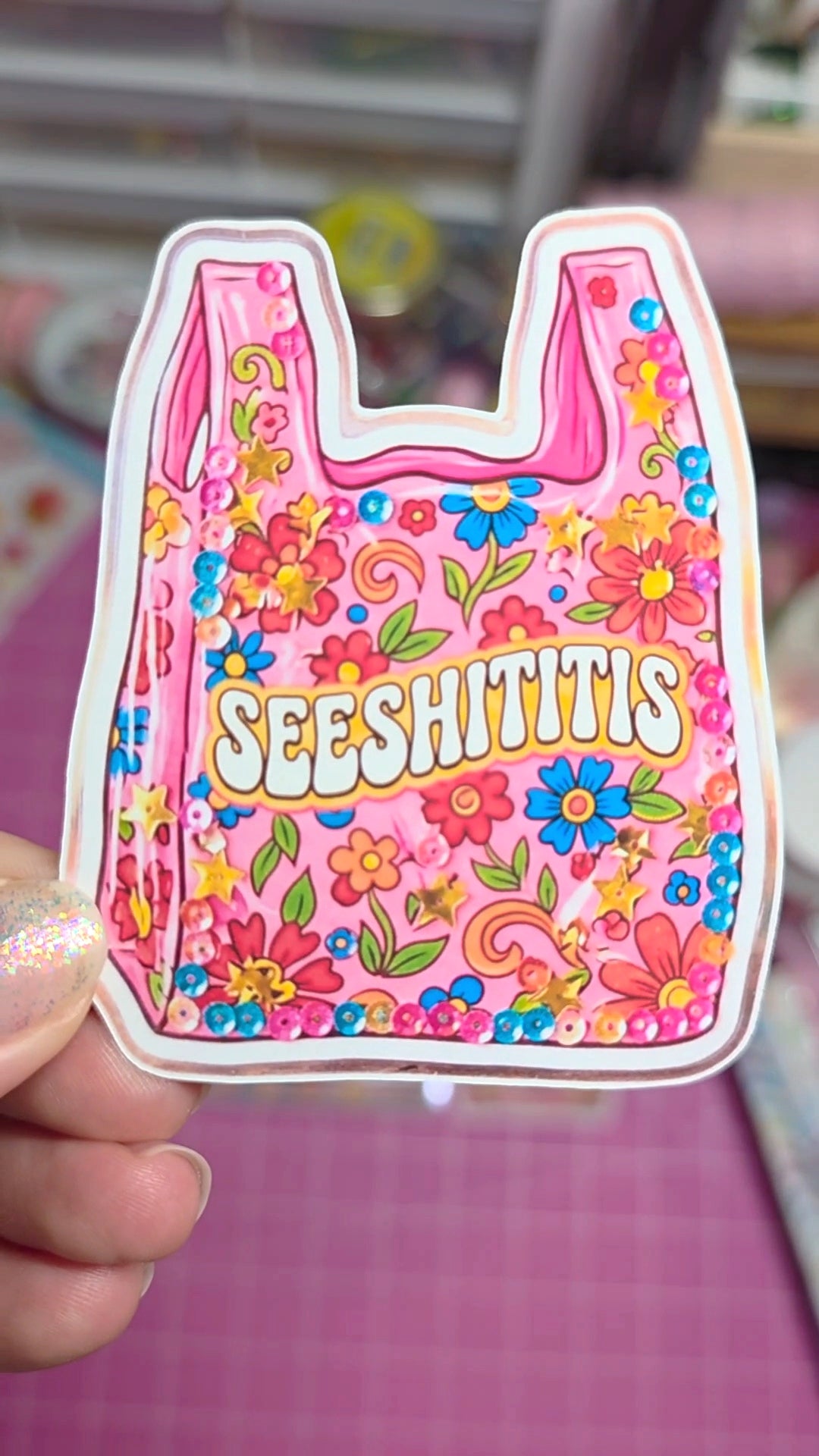 Colorful sticker with floral design and 'SEESHITITIS' text held by a hand.