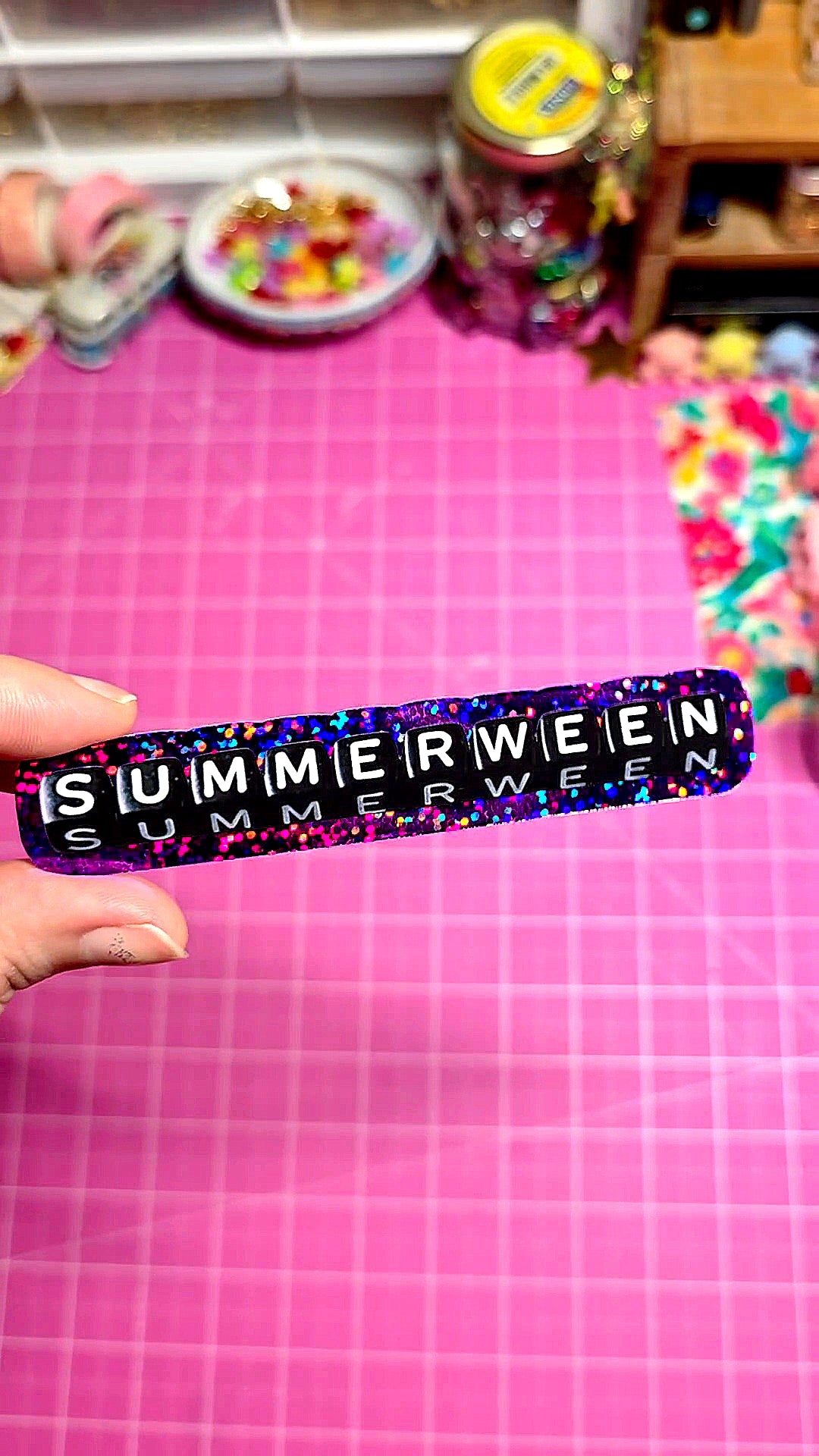 Multicolored 'SUMMERWEEN' band held over a pink checkered background