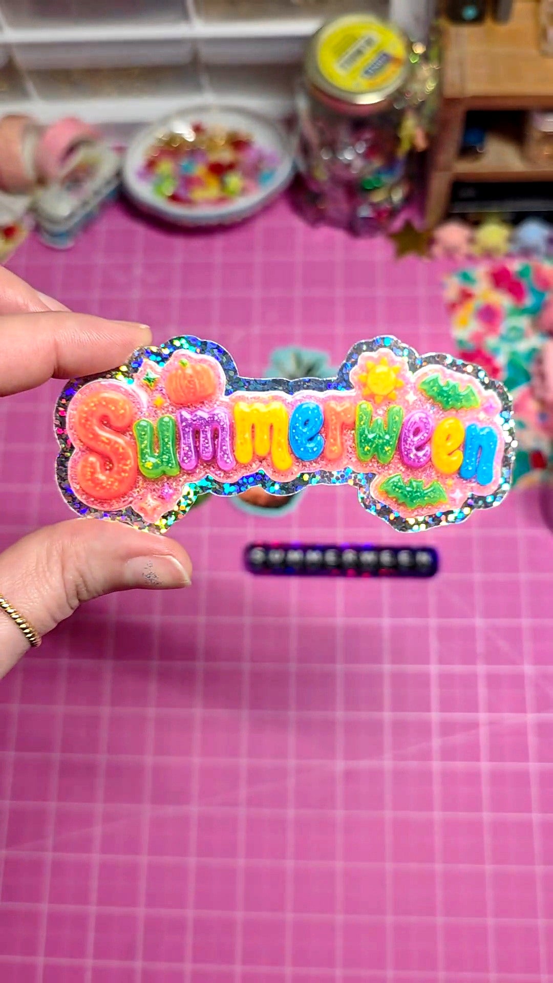 Colorful 'Summer Fun' sticker held over a pink grid background