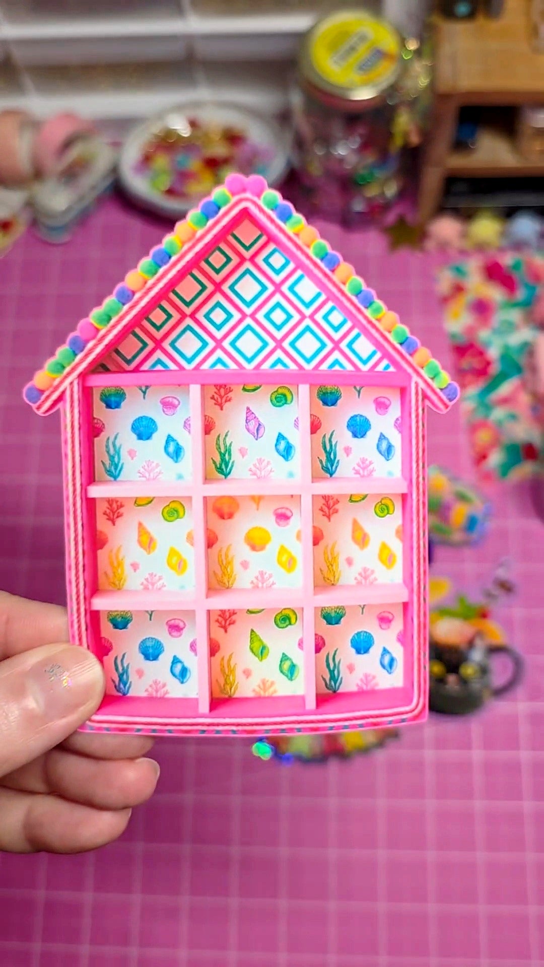 Colorful house-shaped organizer with small compartments on a pink checkered background