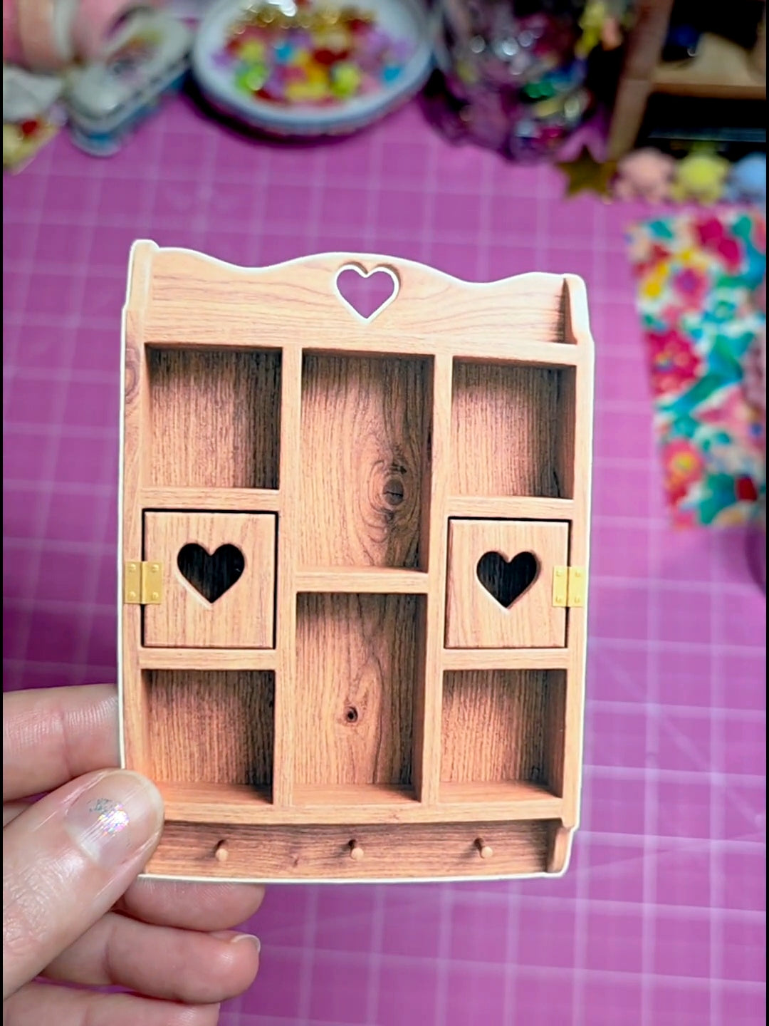 Wooden jewelry box with heart designs held by a hand on a pink grid background