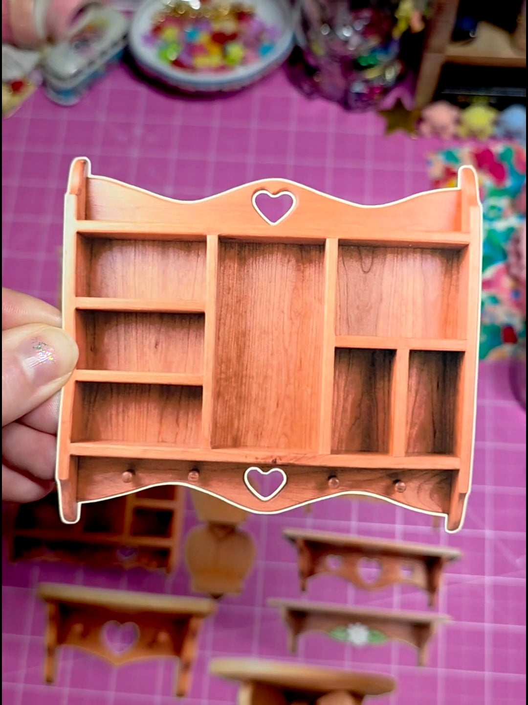 Small wooden shelf with heart designs held by a hand on a pink surface.