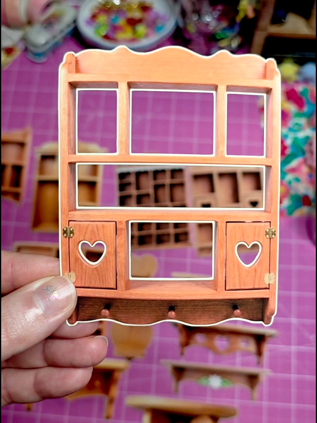 Small wooden cabinet with heart-shaped doors held by a hand against a colorful background