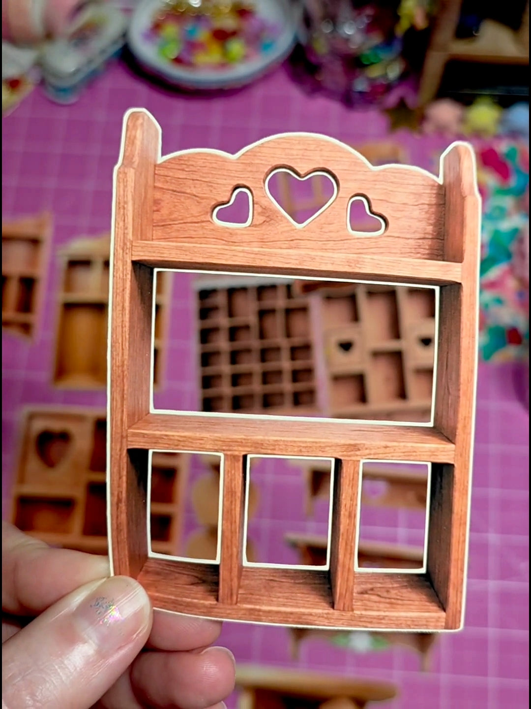 Wooden miniature furniture piece with heart cutouts held by a hand on a colorful background.