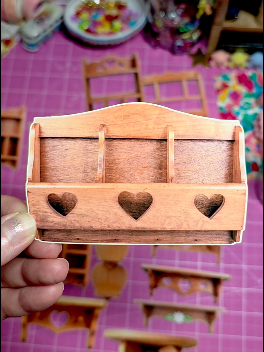 Wooden toy dresser with heart-shaped cutouts held by a hand on a pink surface.