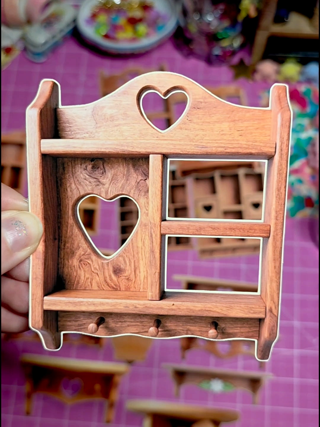 Wooden decorative item with heart shapes held by a hand on a colorful background