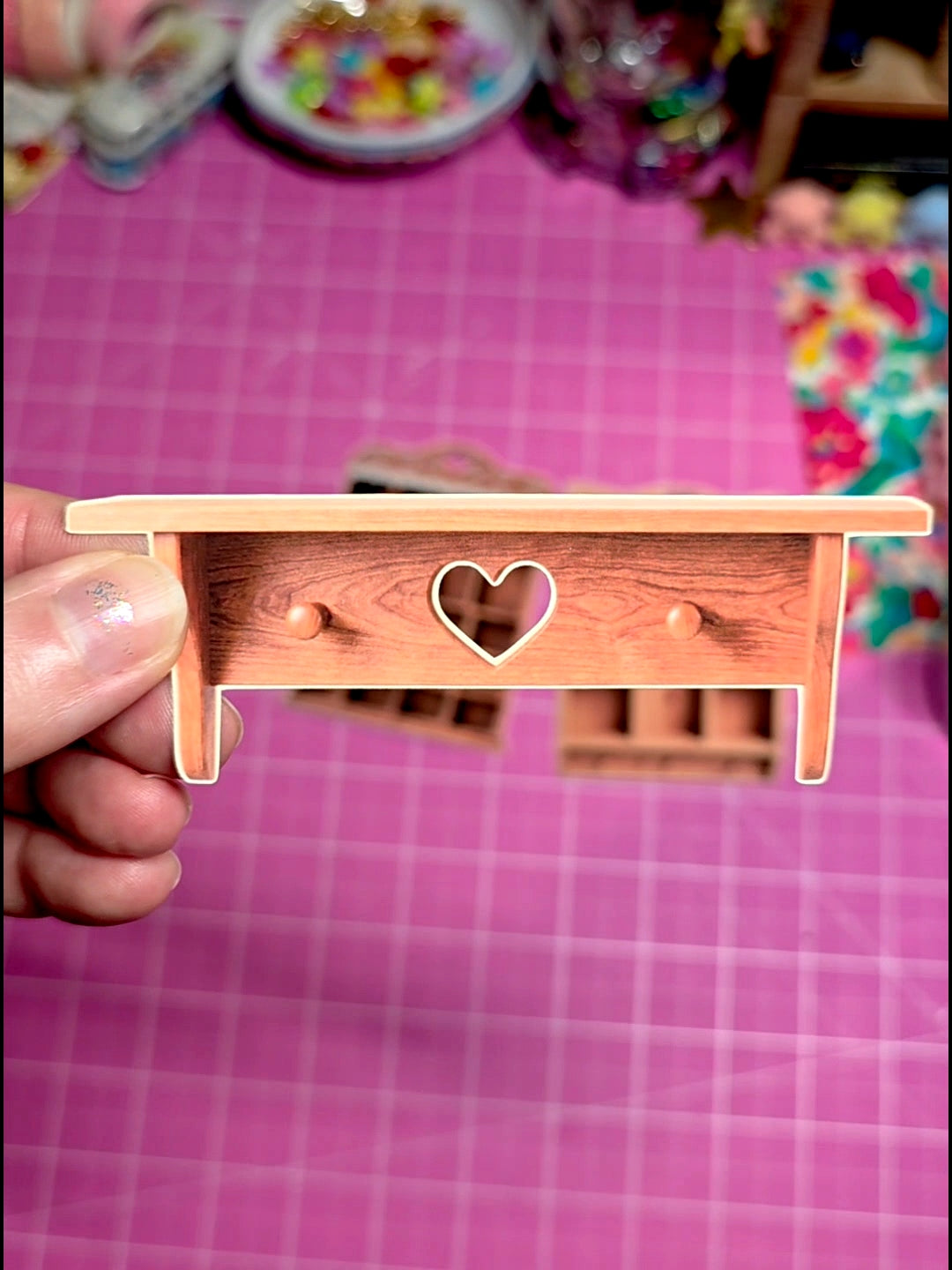 Small wooden shelf with a heart cutout held by a hand on a pink cutting mat.