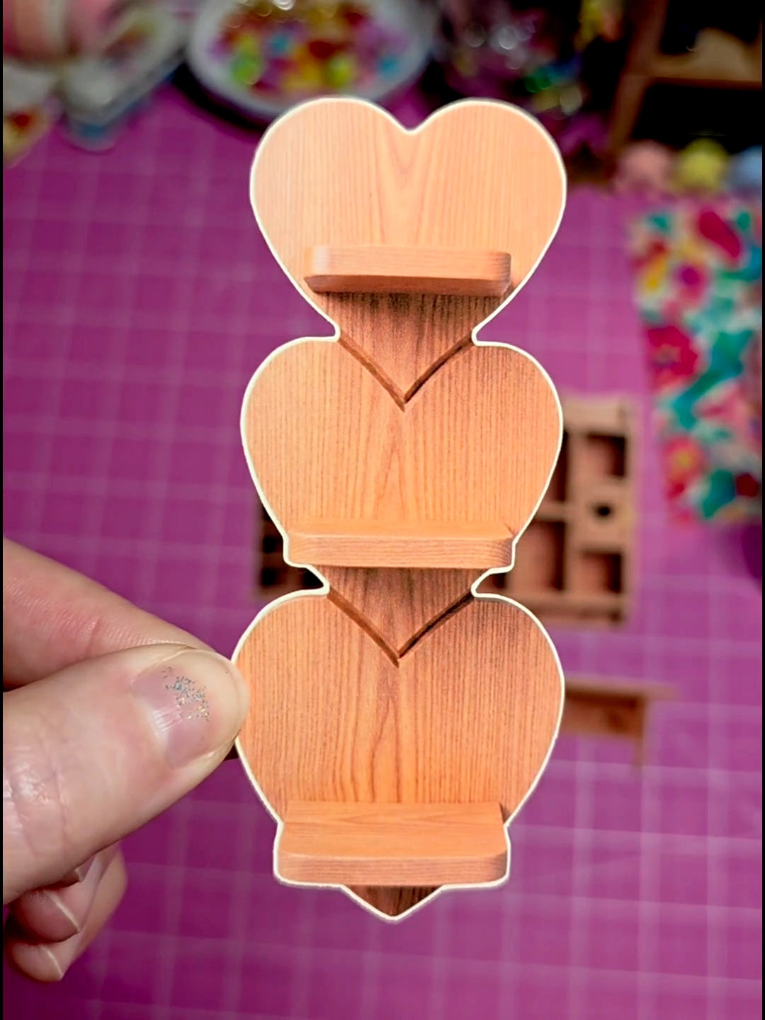 Wooden heart-shaped cookie cutter held by a hand on a pink checkered background